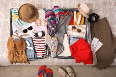 Open suitcase with clothes and accessories on bed indoors, top view
