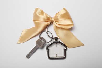 Key with trinket in shape of house and bow on white background, top view. Housewarming party