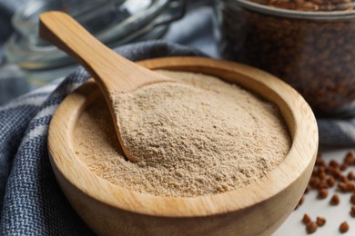 Photo of Buckwheat flour in bowl with wooden spoon on white table, closeup