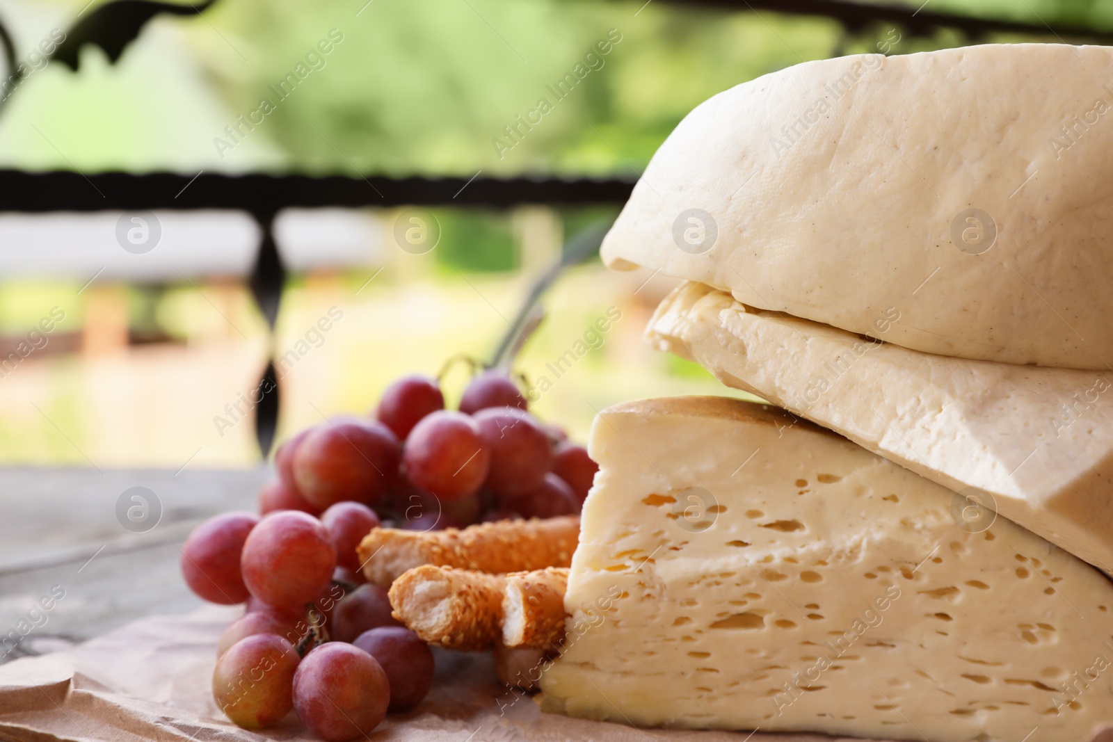 Photo of Delicious cheese, bread and ripe grape on wooden table, closeup