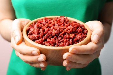 Photo of Woman holding bowl of red dried goji berries, closeup