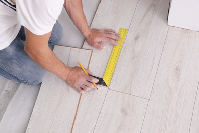 Man using measuring tape during installation of laminate flooring, above view