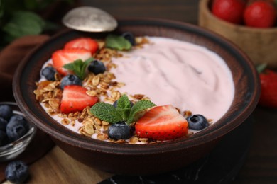 Bowl with yogurt, berries and granola on wooden table, closeup