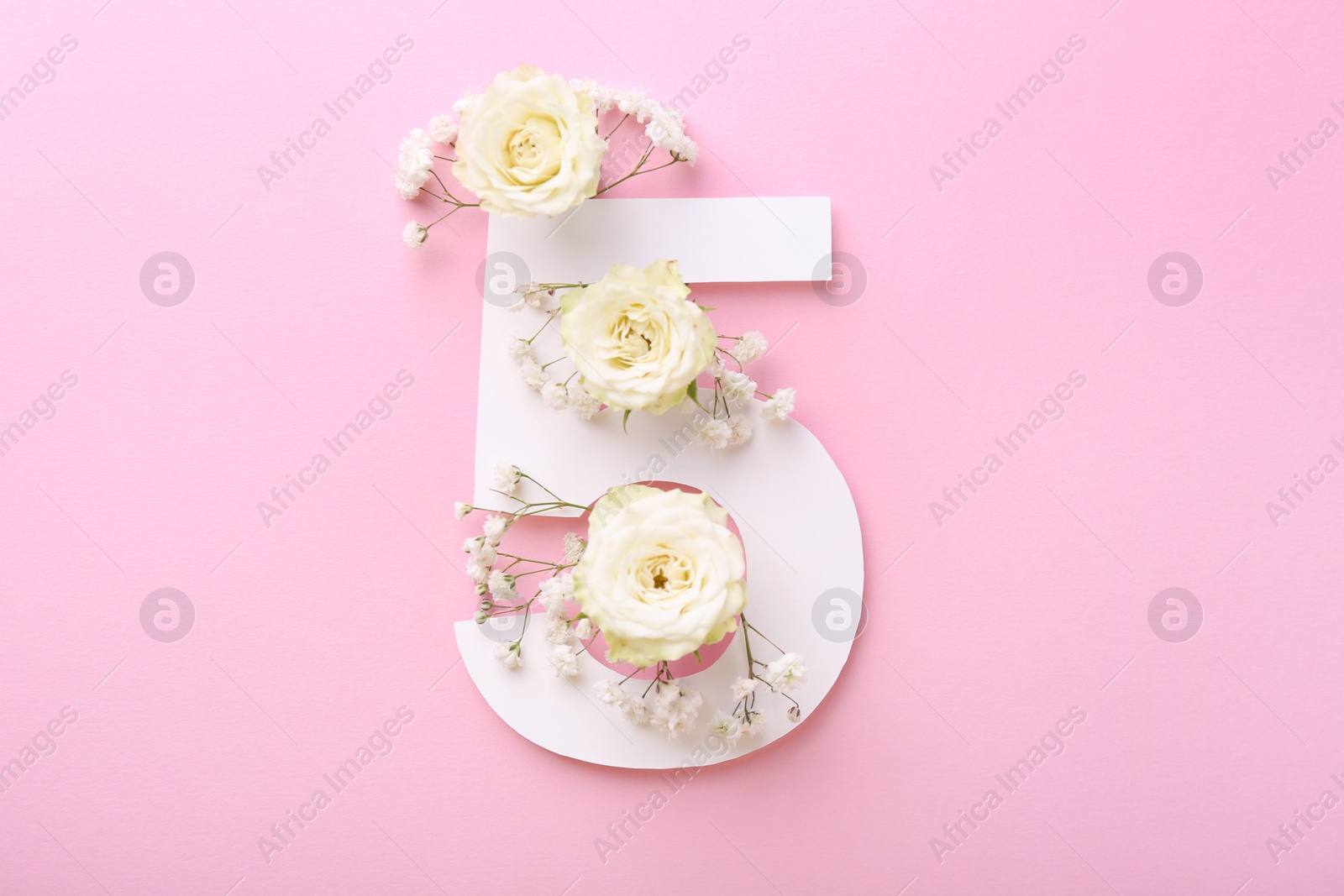 Photo of Paper number 5 and beautiful flowers on pink background, top view