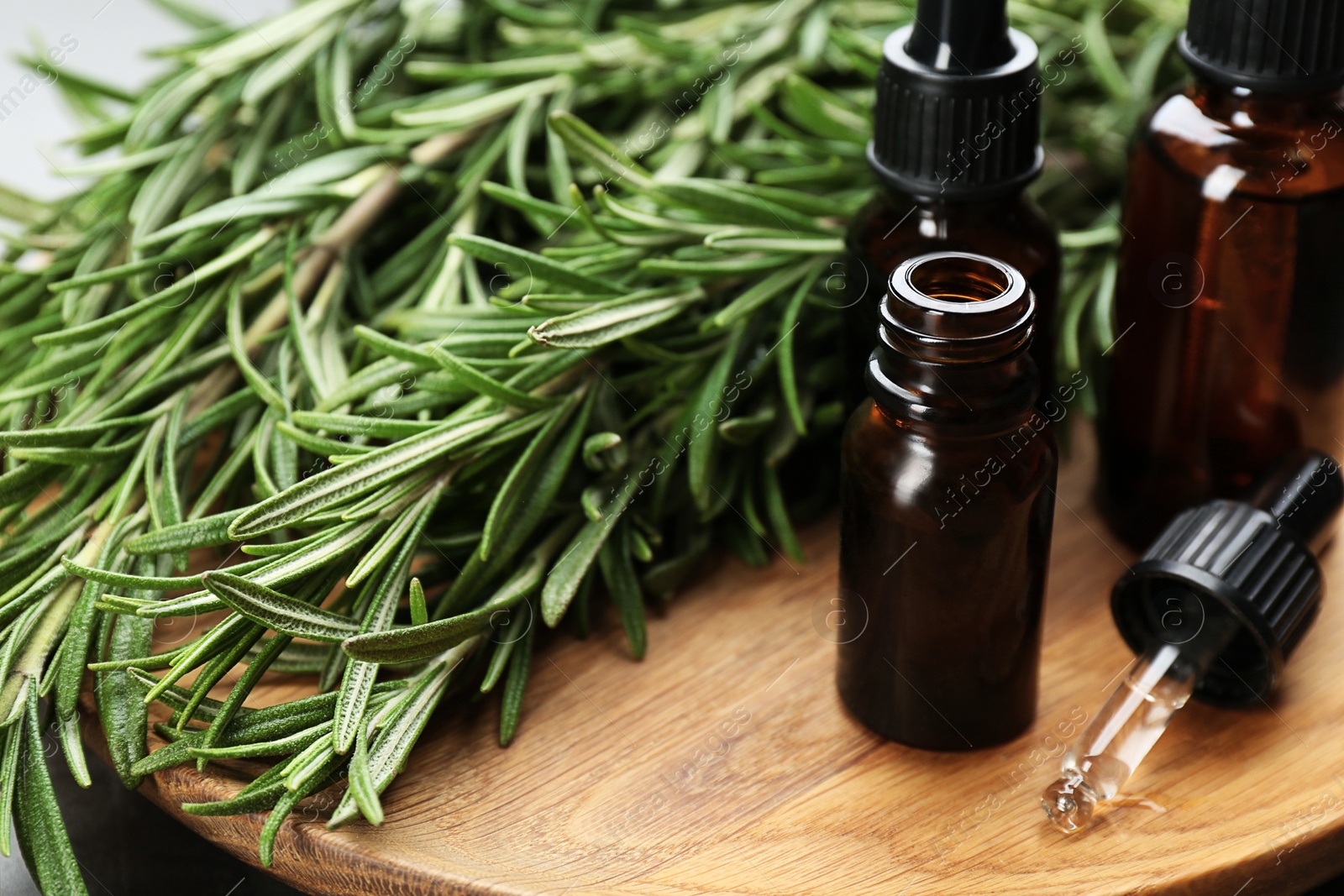 Photo of Fresh rosemary and bottles of essential oil on wooden plate, closeup