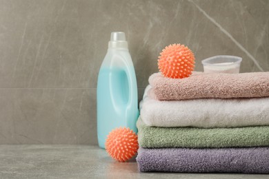 Photo of Dryer balls, detergents and stacked clean towels on grey marble table. Space for text