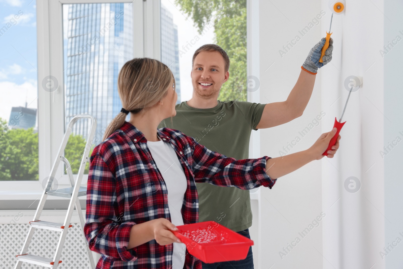 Photo of Happy couple painting wall in apartment during repair