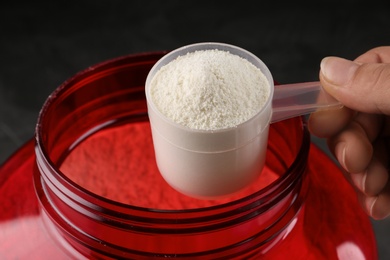 Photo of Woman holding measuring scoop of protein powder over jar, closeup