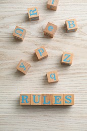 Photo of Word Rules made of cubes with letters on light wooden table, flat lay