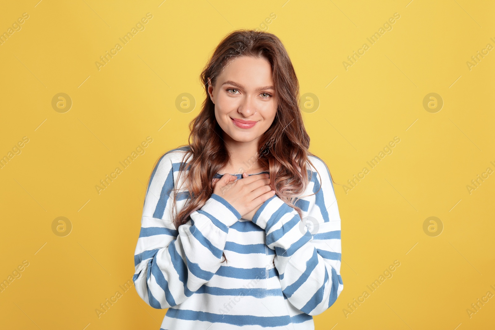 Photo of Beautiful grateful woman with hands on chest against yellow background