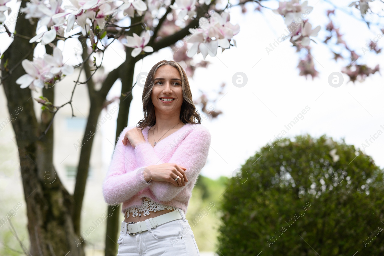 Photo of Beautiful young woman near blossoming magnolia tree on spring day, space for text