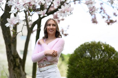 Beautiful young woman near blossoming magnolia tree on spring day, space for text