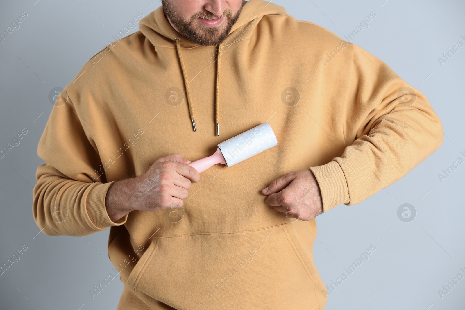 Photo of Young man cleaning clothes with lint roller on grey background, closeup