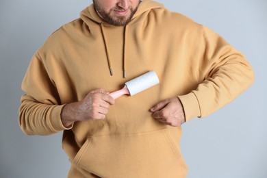 Young man cleaning clothes with lint roller on grey background, closeup