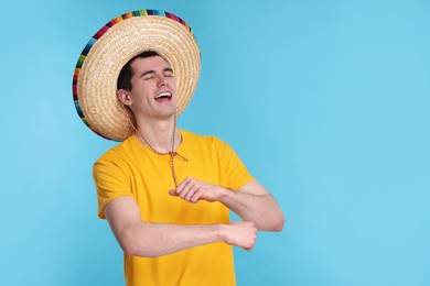 Photo of Young man in Mexican sombrero hat dancing on light blue background. Space for text