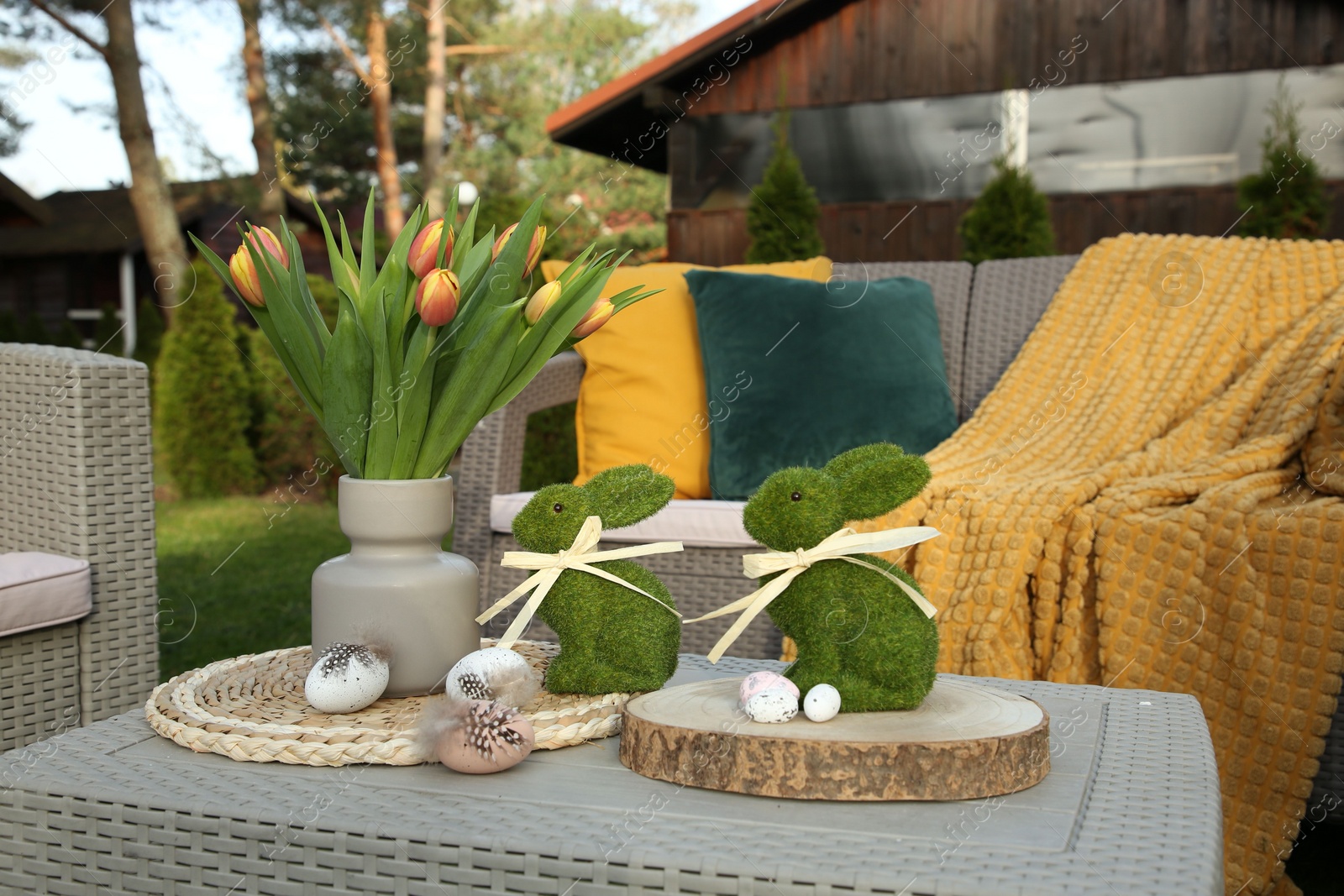 Photo of Terrace with Easter decorations. Bouquet of tulips in vase, bunny figures and decorative eggs on table outdoors