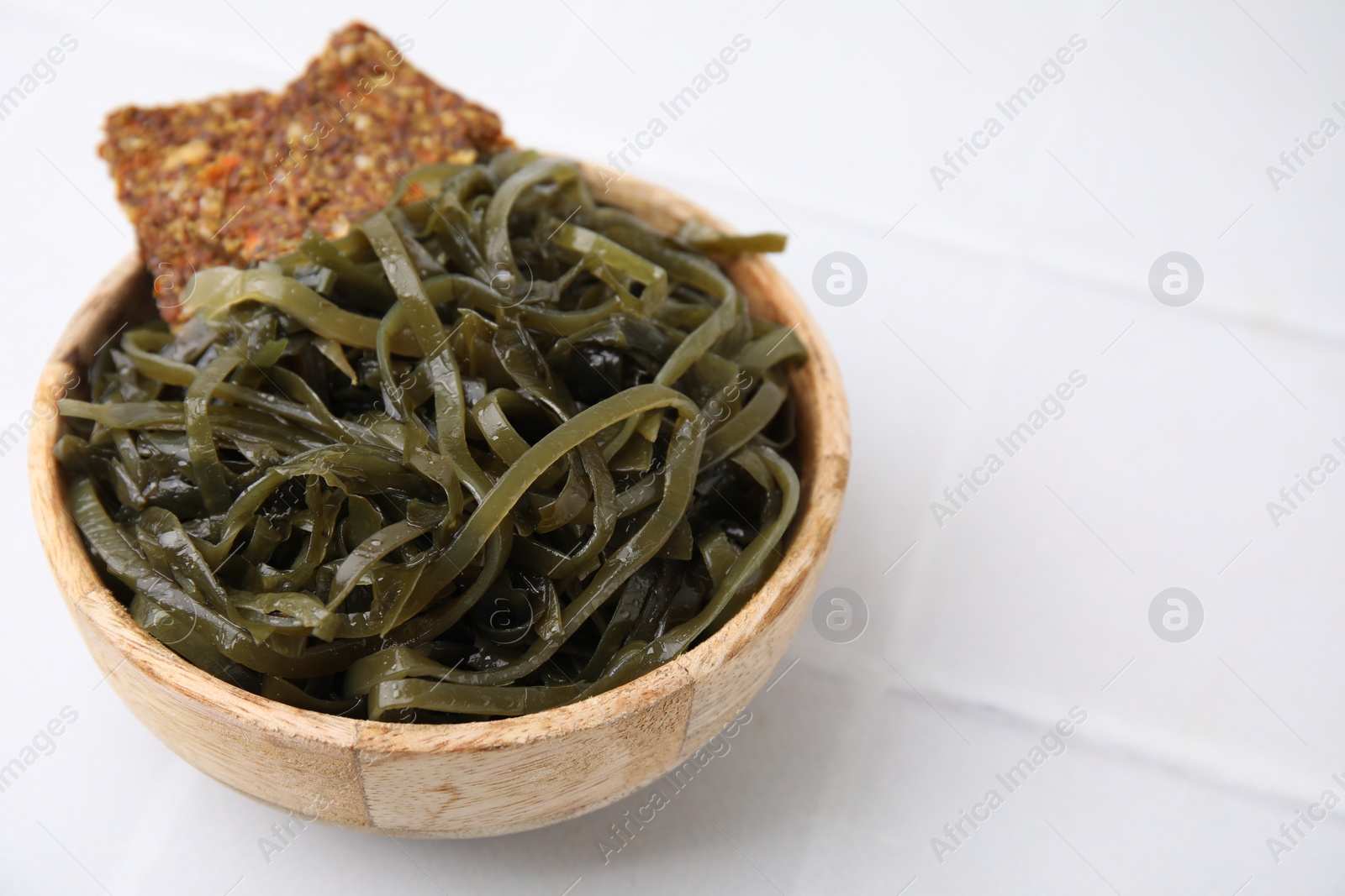 Photo of Tasty seaweed salad and crispbreads in bowl on white tiled table, closeup. Space for text