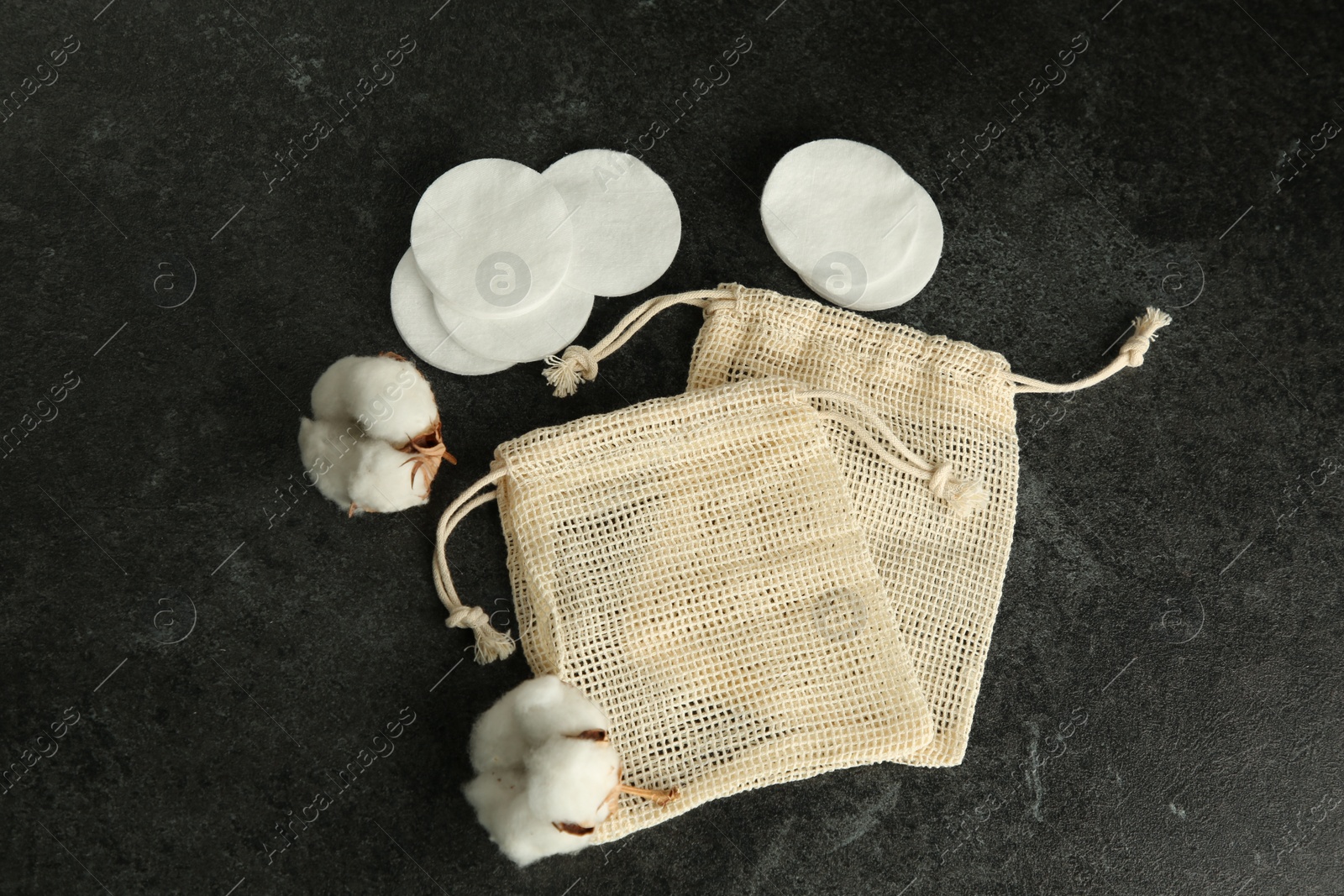 Photo of Cotton pads, bag and flowers on black table, flat lay