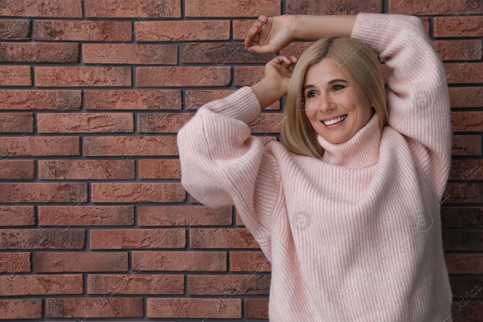 Photo of Happy woman in stylish sweater near brick wall. Space for text