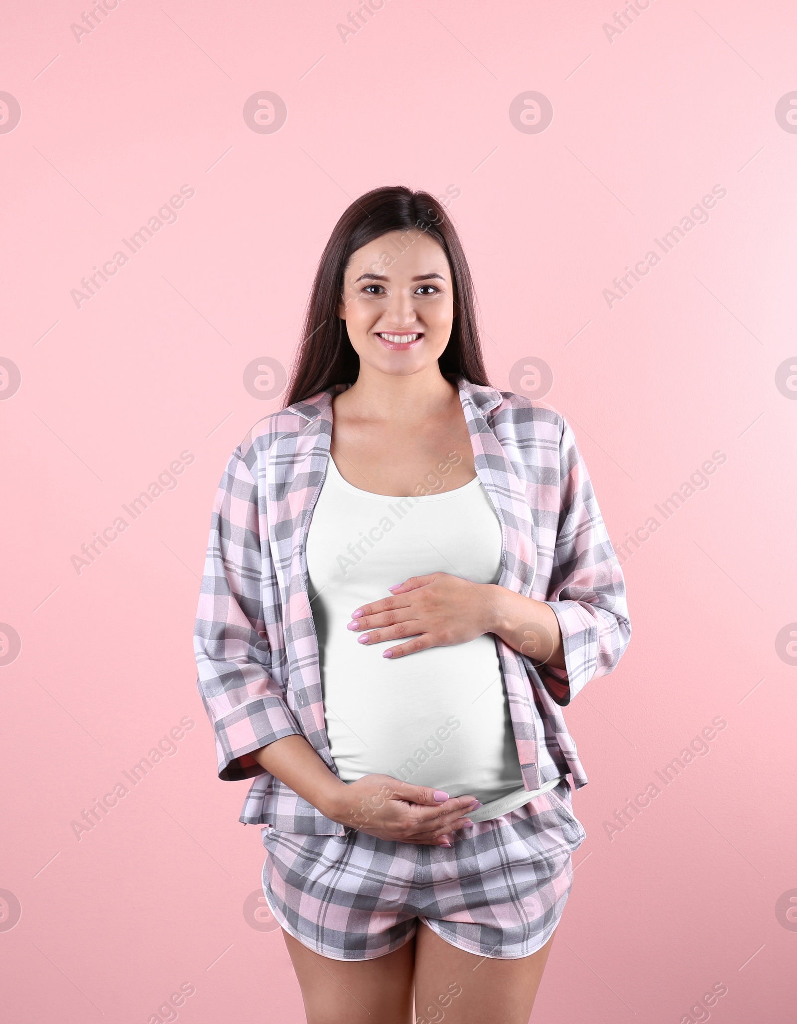 Photo of Beautiful pregnant woman holding hands on belly against color background