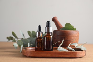 Photo of Aromatherapy. Bottles of essential oil and eucalyptus leaves on brown table, closeup