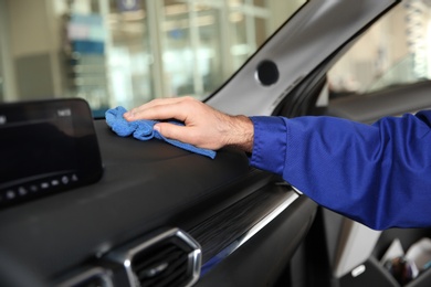 Photo of Worker cleaning automobile dashboard with rag at car wash, closeup