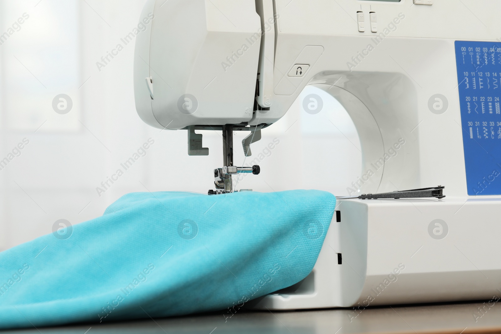 Photo of Sewing machine with fabric and tailor's scissors on wooden table indoors, closeup