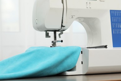 Sewing machine with fabric and tailor's scissors on wooden table indoors, closeup