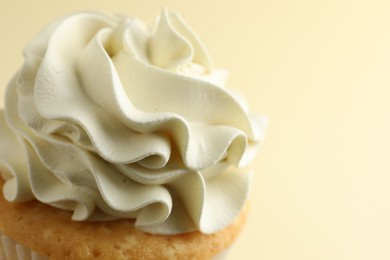 Tasty vanilla cupcake with cream on pale yellow background, closeup. Space for text