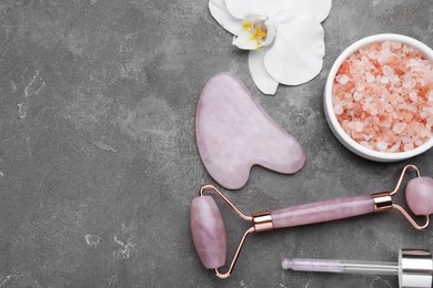 Photo of Gua sha stone, face roller, cosmetic products and orchid flower on grey table, flat lay. Space for text