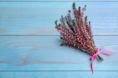 Bunch of heather branches with beautiful flowers and ribbon on light blue wooden table, top view. Space for text