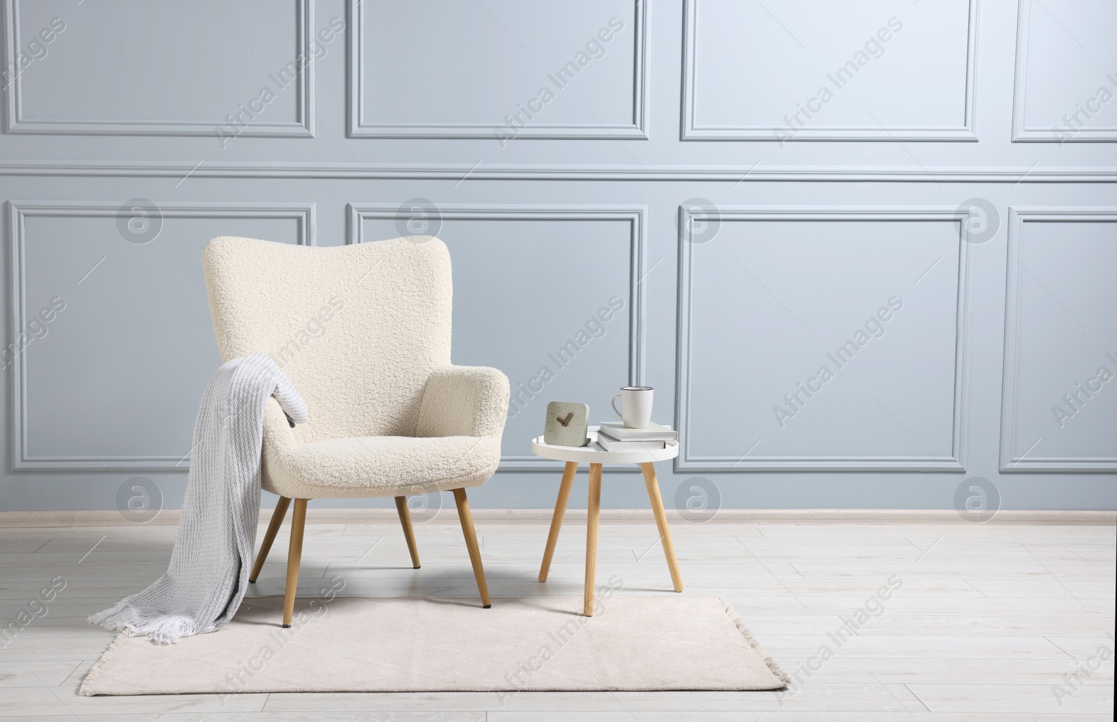 Photo of Comfortable armchair with blanket and side table indoors, space for text