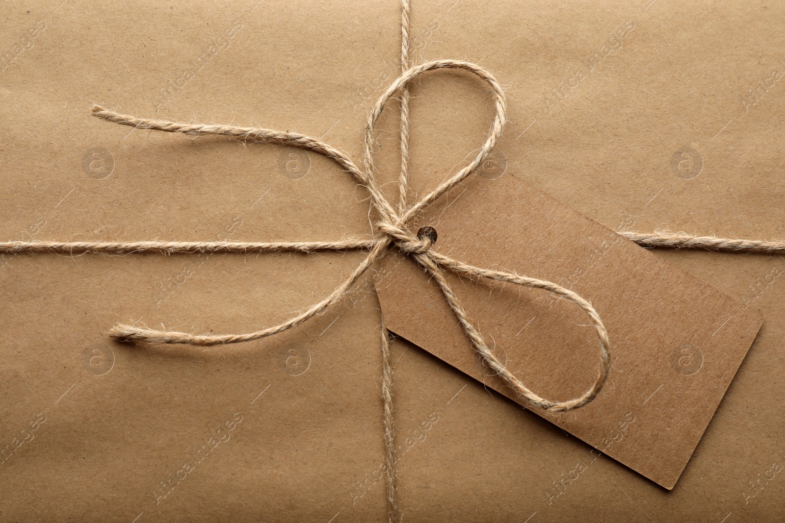 Photo of Parcel wrapped in kraft paper with tag as background, closeup