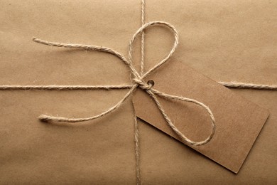 Photo of Parcel wrapped in kraft paper with tag as background, closeup