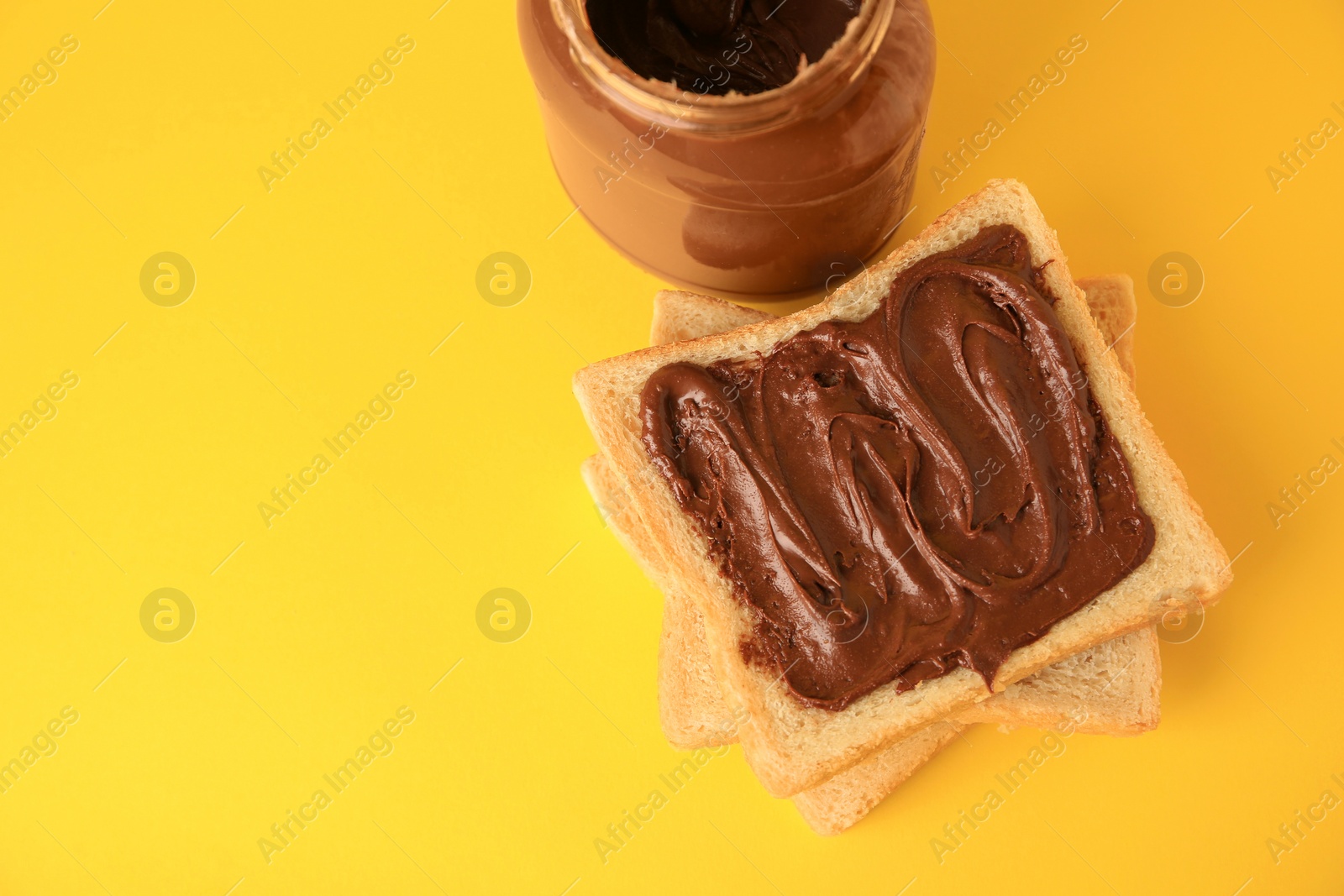 Photo of Tasty toast with chocolate paste and jar of cream on yellow background, above view. Space for text