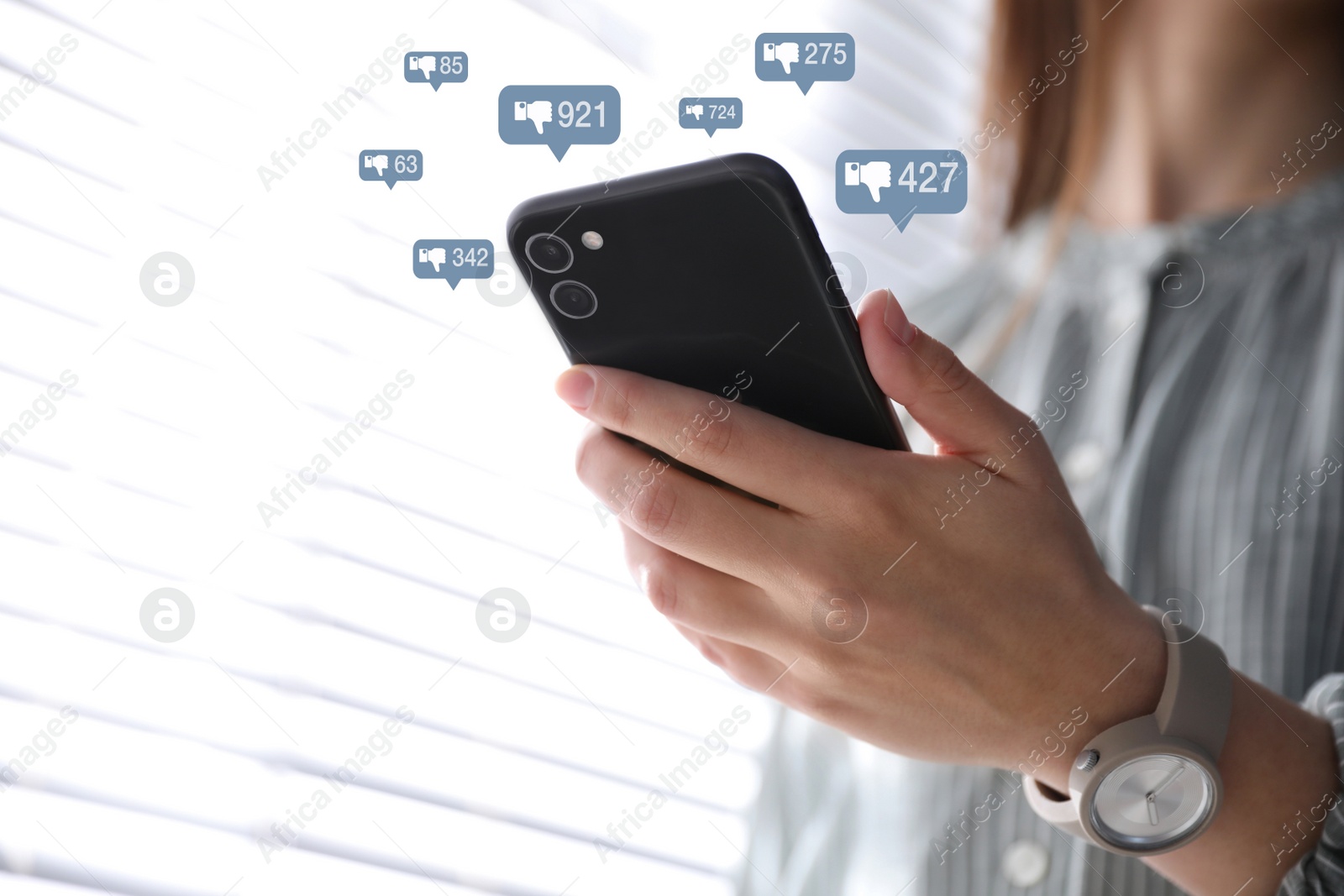 Image of Closeup view of young woman using modern smartphone indoors and virtual dislike icons. Cyberbullying concept