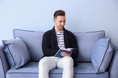 Photo of Young man sitting on sofa and reading book, indoors