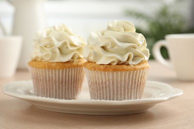 Photo of Tasty cupcakes with vanilla cream on light wooden table, closeup