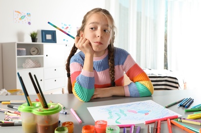 Photo of Little girl drawing picture at table with painting tools indoors