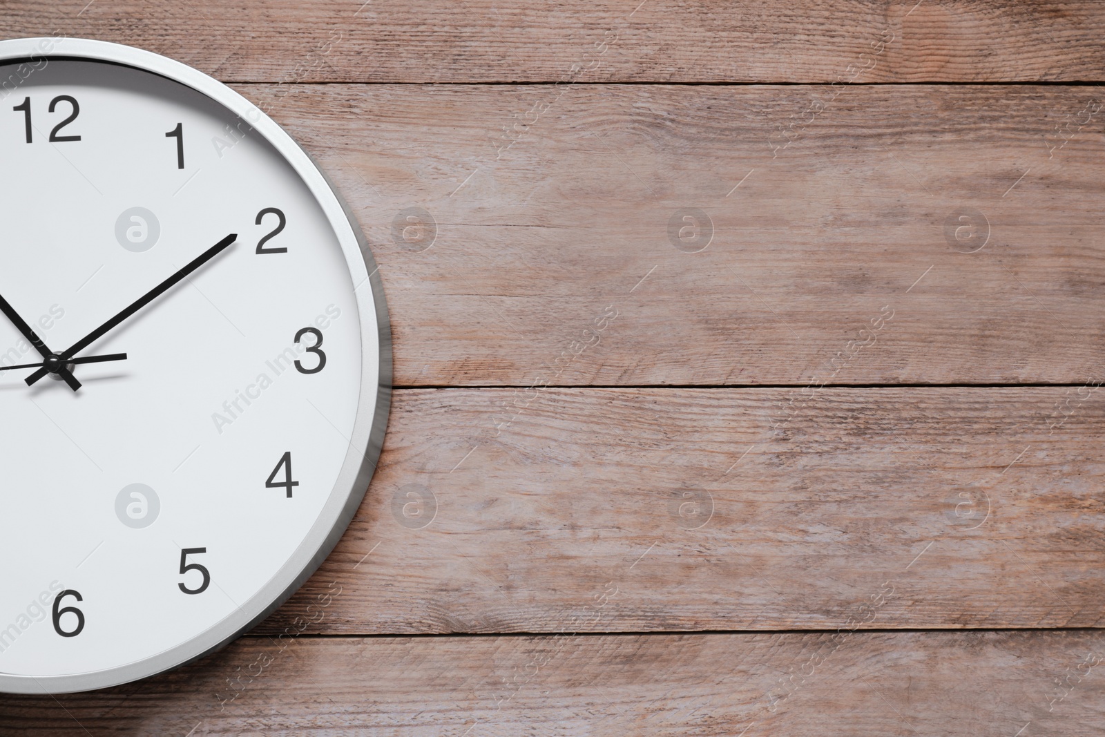 Photo of Stylish round clock on wooden table, top view with space for text. Interior element