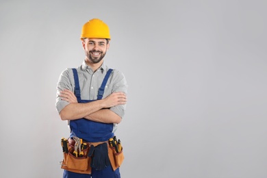 Photo of Portrait of professional construction worker with tool belt on grey background, space for text