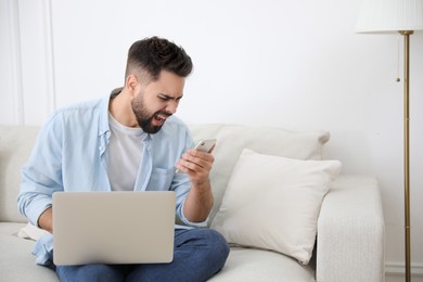 Photo of Emotional young man with laptop and smartphone at home. Online hate concept