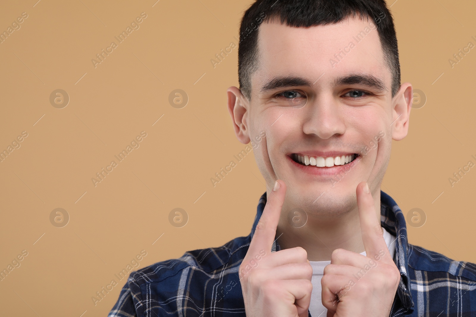 Photo of Handsome young man showing his clean teeth on beige background, space for text