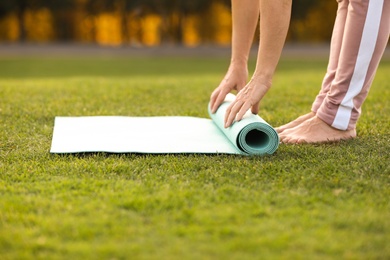 Photo of Mature woman unrolling yoga mat outdoors, closeup