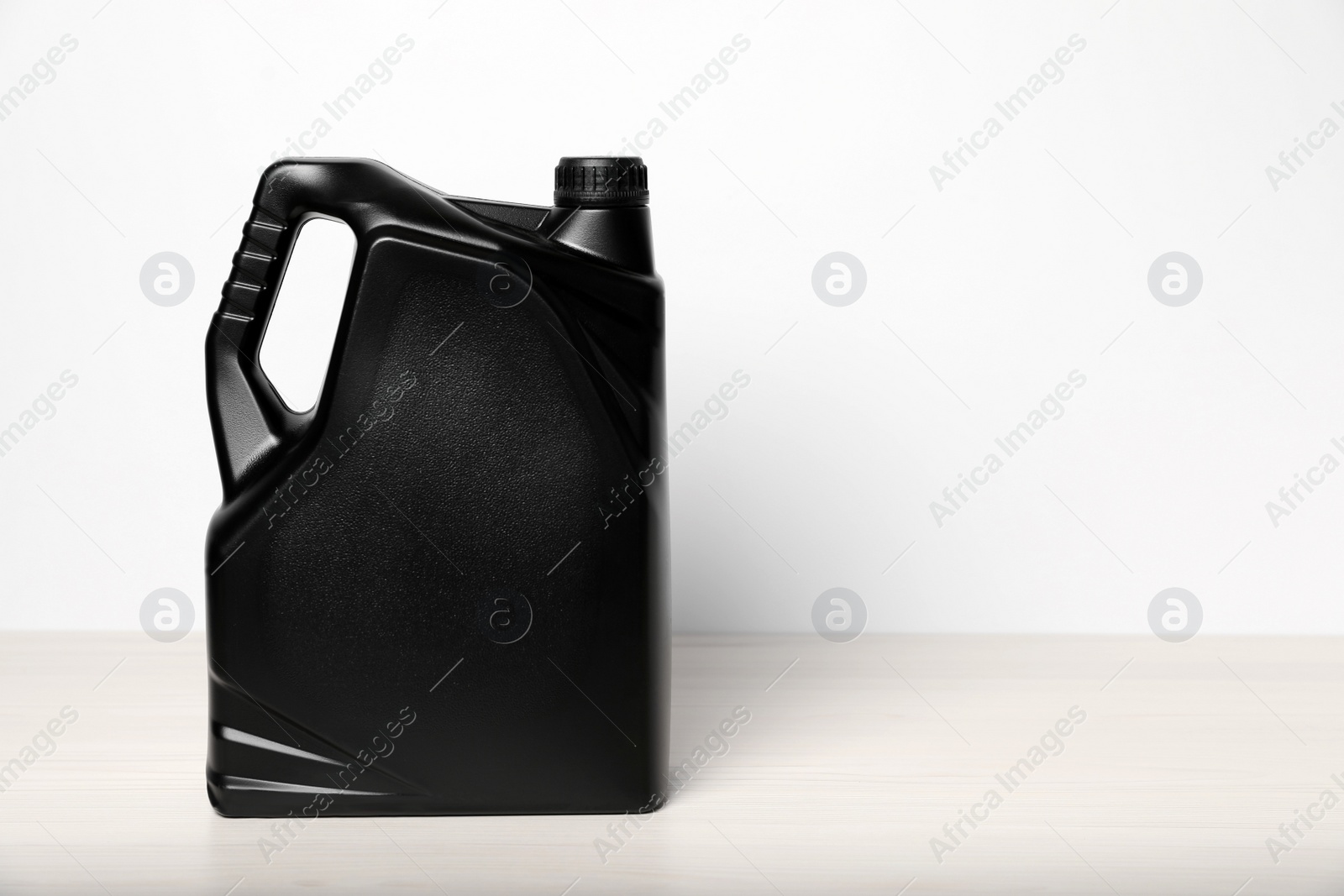 Photo of Motor oil in black canister on table against white background, space for text