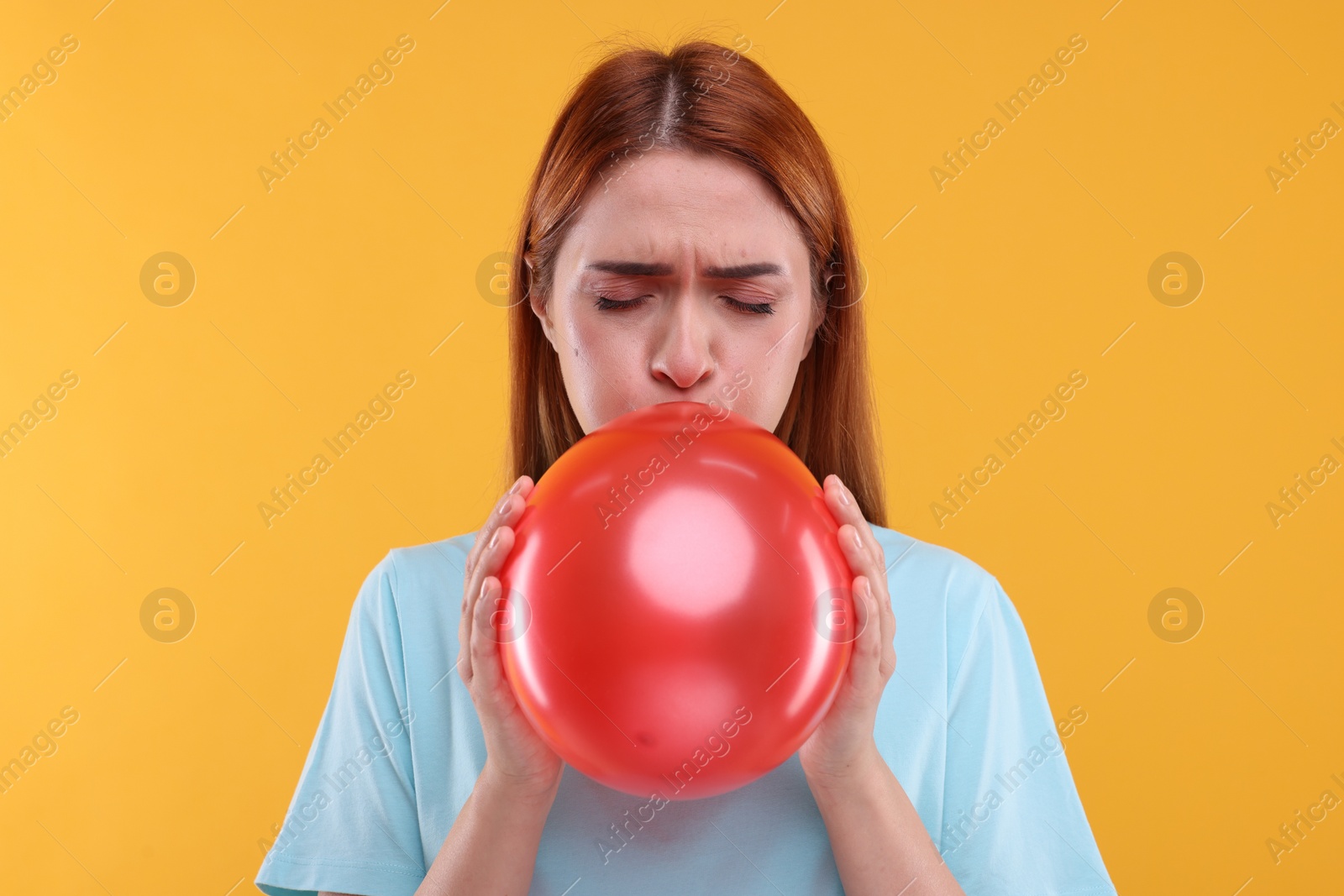 Photo of Woman inflating red balloon on orange background