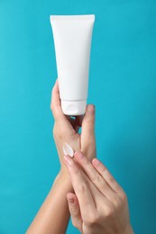 Photo of Woman with tube applying cosmetic cream onto her hand on light blue background, closeup