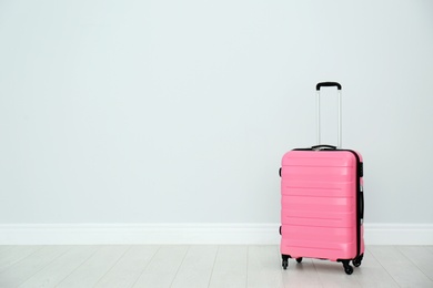 Photo of Modern suitcase on floor near light wall. Space for text