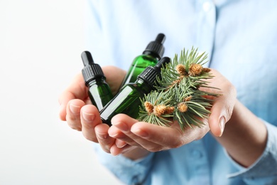 Photo of Woman holding bottles of essential oils and fir branches on white background, closeup