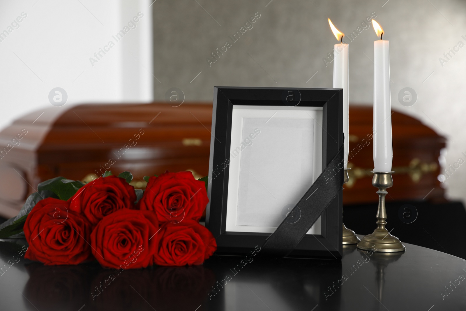 Photo of Black photo frame with burning candles and red roses on table in funeral home